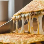 Cheeseburger quesadilla wedge lifted with melted cheese stretching out