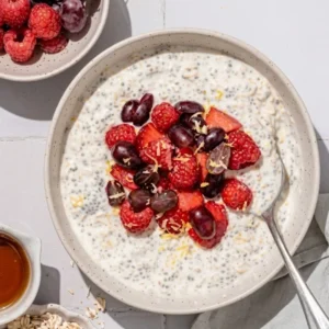 Overhead view of a ceramic bowl filled with creamy chia overnight oats topped with raspberries, blueberries, and lemon zest.